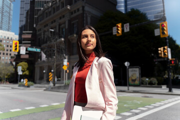 Beautiful stylish Indian businesswoman holding laptop walking on urban street. Successful business 