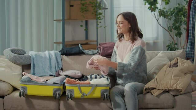 A Smiling Young Woman Traveler Gathers Clothes for a Trip, Packs Things into a Suitcase at Home. Island Adventures. Water Sports.