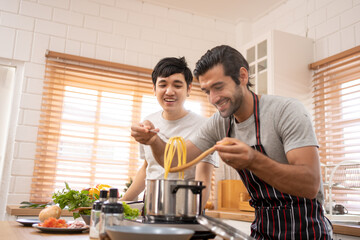 Two guys of different ethnicity having fun while making spagghetti together on kitchen. Concept of gay LGBTQ couples and everyday life at home . Asian and hispanic man cooking healthy food.