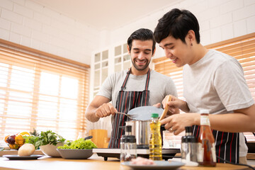 Obraz na płótnie Canvas Two guys of different ethnicity having fun while making spagghetti together on kitchen. Concept of gay LGBTQ couples and everyday life at home . Asian and hispanic man cooking healthy food.