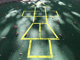 Painted yellow lines contrast against the dark asphalt and form the classic school playground game of Hopscotch