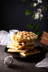 Pile of Fresh Homemade soft waffles served on dark plate.