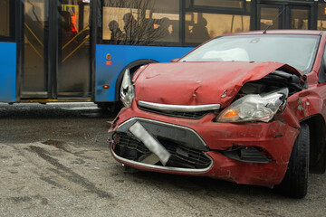 A car wrecked in an accident stands on the road against the background of a bus passing by.