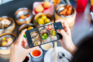 Young woman traveler taking a photo of  traditional Chinese Dim Sum at restaurant while traveling