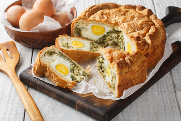 Torta Pasqualina is an traditional Italian Easter speciality made of puff pastry, ricotta cheese, spinach and eggs closeup on the wooden board on the table. Horizontal