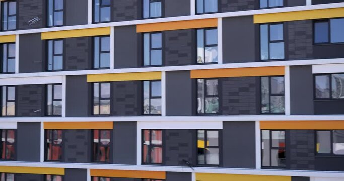 The windows of a high-rise building with gray and yellow slats on the front of the building. Zoom in for a close-up. The windows of the house reflect the sky and the facade of another house.   
