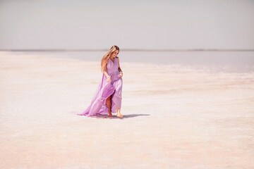Woman pink salt lake. Against the backdrop of a pink salt lake, a woman in a long pink dress takes...