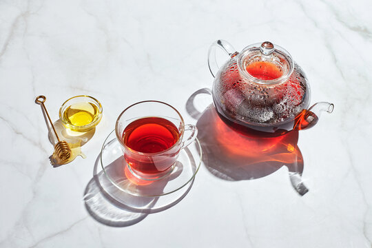 Fruit Tea With Apples And Thyme And Honey In Glass Teapot And Cup On White Background With Hard Shadows