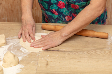 Elderly woman kneading dough on a wooden table in the kitchen