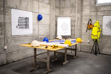Construction site meeting room with desk, blueprints, plant and helmets.