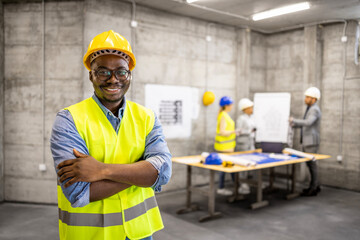 Construction worker with crossed arms standing at building site.