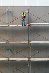 Construction worker on the scaffold prepares house facade wall for painting