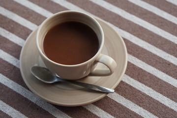 closeup hot latte coffee in a ceramic cup and silver spoon on a ceramic coaster on brown and white fabric background, drink, food, health, copy space