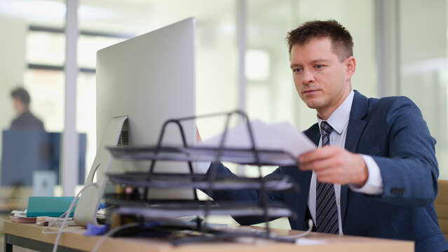 Businessman taking out paper from tray on desk in office. Working with documents concept