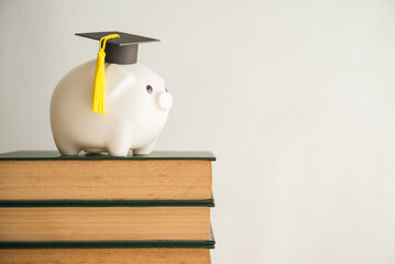 Piggy bank and graduation cap on stack textbooks in classroom with white wall background copy space. Personal financial planning and money management for education, abroad educational, money savings.