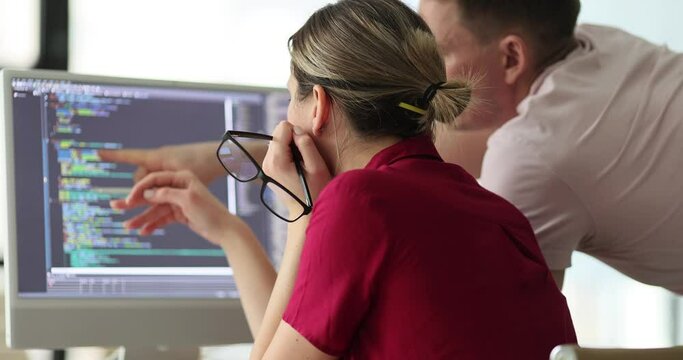 Programmers discuss code structure at table with monitor in office. Project manager with engineer checks up digital data. Concept of developing systems support at work slow motion