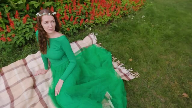 Fairy woman sits on the grass in the park. Fairy in a green dress.