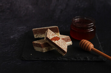 milk-chocolate halva with sesame seeds and nuts in pieces on a board on a dark background