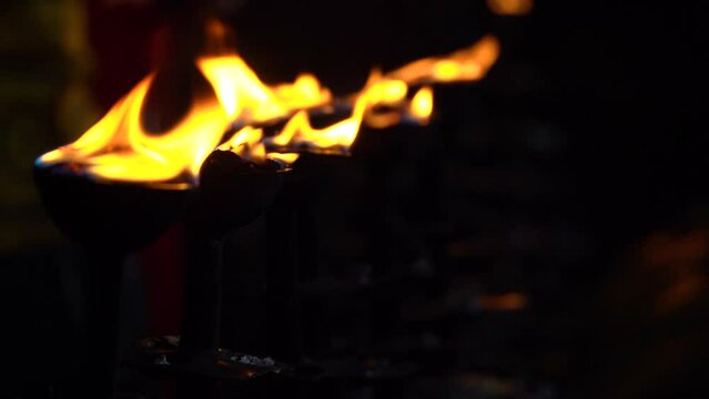close up shot of fire burning in diyas holy lamps kept on the bank of river ganga with people passing around it seeking blessings in the holy city of rishikesh