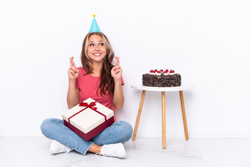 Young Russian girl celebrating a birthday sitting one the floor isolated on white background with fingers crossing