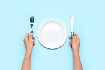 Female hands with empty plate and cutlery on blue background