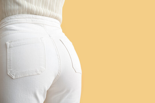 Young woman in white jeans on yellow background, back view