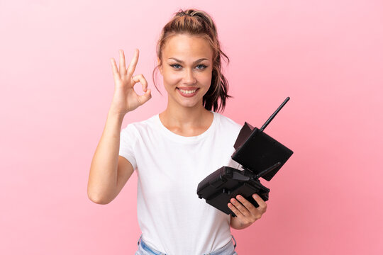 Teenager Russian girl holding a drone remote control isolated on pink background showing ok sign with fingers