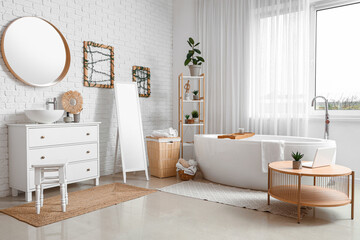 Interior of light bathroom with bathtub, mirror and chest of drawers