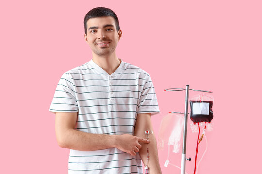 Young man donating blood on pink background