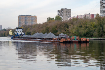 Barge loaded with sand or grey gravel floats on wide river