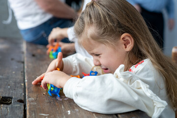 Capricious, dissatisfied, greedy little girl cries, mumbles and plays with balancing colorful chairs trying to build stable tower out of them