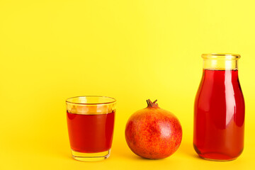 Bottle and glass of fresh pomegranate juice on yellow background