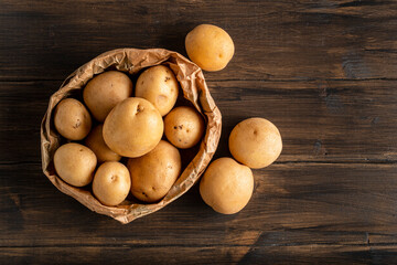 Fresh yellow potatoes in a paper bag on a wooden background. - obrazy, fototapety, plakaty