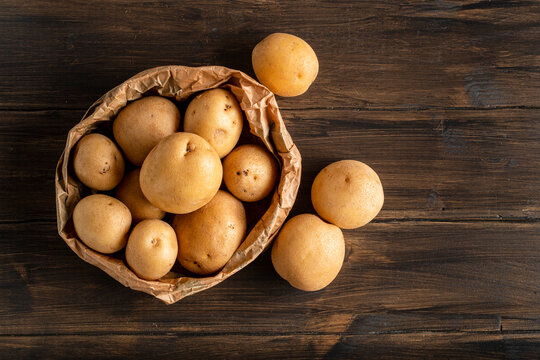 Fresh yellow potatoes in a paper bag on a wooden background.