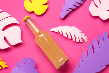 Composition with bottle of fresh soda and paper leaves on pink background