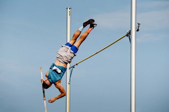 male athlete jumping pole vault in summer athletics championships on background blue sky