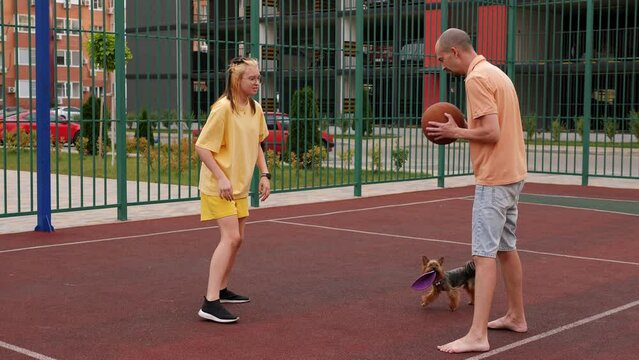 Happy father and teenage daughter play basketball outdoors on the court. The family plays sports in the courtyard of a modern residential complex.