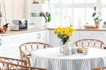 Vase with flowers, teapot, cups and croissants on dining table in kitchen