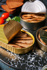 Board of canned smoked sprats on dark background