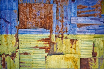 Flag of Ukraine painted onto rusty corrugated iron sheets overlapping to form a wall or fence