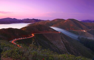 Fototapeta na wymiar Long exposure of cars driving along the mountain trail in the Marin headlands at a foggy sunset