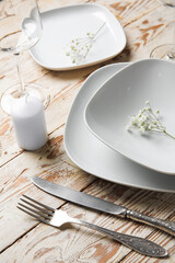Beautiful table setting with candle and gypsophila flowers on light wooden background, closeup