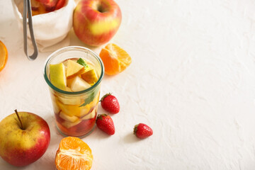 Glass of infused water with different sliced fruits on white table