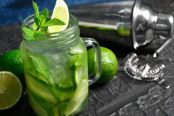 Mason jar of cold mojito and shaker with lime on black table