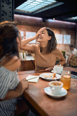 Two young girlfriends at cafe having fun and laughing, talking. Coffee break, lunch, togetherness concept.