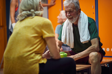 Senior man and woman having a joyful conversation in gym locker room after workout.