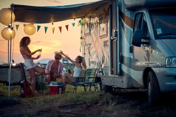 Fotobehang Three friends toasting and having fun outdoors, in front of camper rv. Summertime sunset. Travel, holiday, weekend, togetherness, lifestyle concept. © luckybusiness