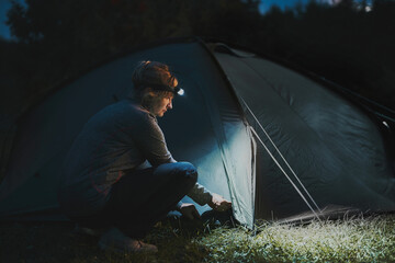 Summer vacation. Woman opening tent at camping in the evening using head lamp. Summer trip....