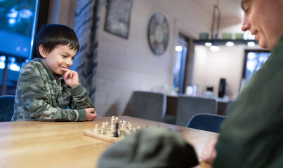 Military man in olive uniform playing chess and having fun with his little son at home