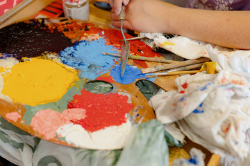 A young girl holds in his hand a palette-knife for drawing and mixes oiled paints. The process of mixing colors on the palette.